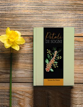 Closed green book and yellow daffodil flower on wooden background, top view, copy space.